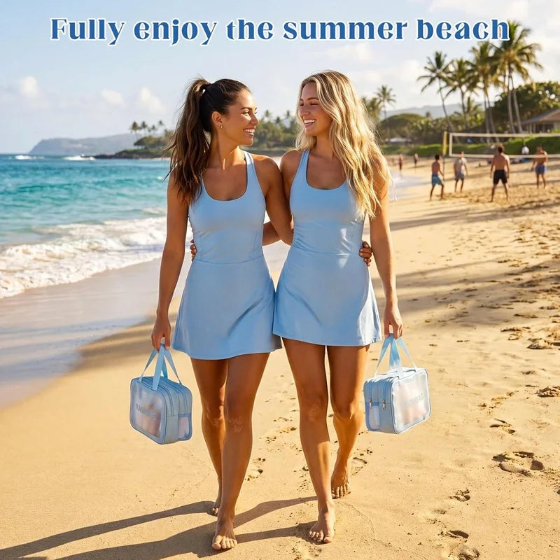 Two women walk along a sunny beach holding blue travel toiletry bags.