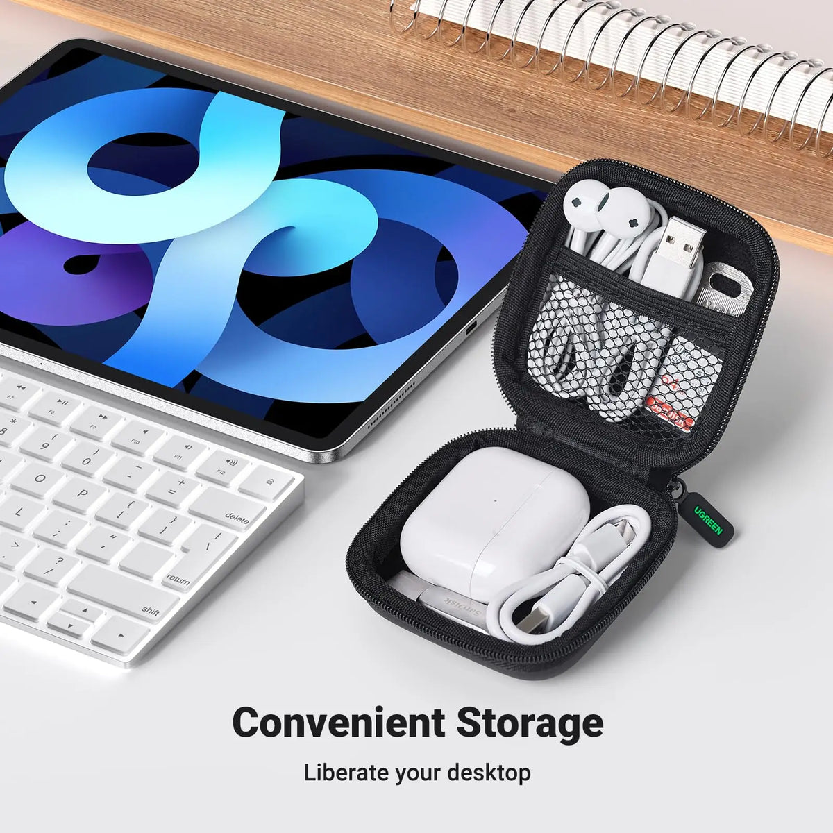 Una caja de almacenamiento negra contiene AirPods blancos y accesorios junto a una laptop plateada.