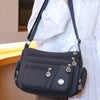 A black waterproof nylon crossbody tote bag with gold hardware is shown against a white shirt.