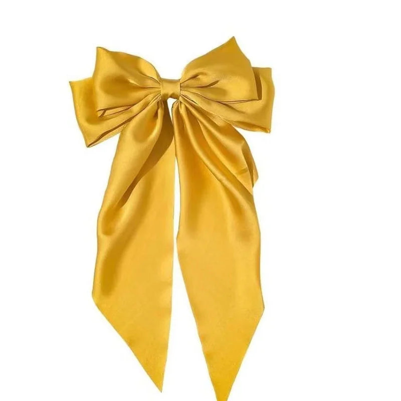 A golden yellow silk bow used as a hair accessory for a ponytail.