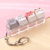 A row of pink and white kawaii cat keycaps fidget toys displayed on a clear plastic tray with a silver bag charm.