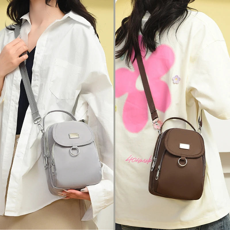 Une femme tient un sac bandoulière floral gris contre un chemisier blanc.