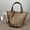 A tan genuine leather bucket bag with a handle is displayed on a gray surface next to a light fabric pouch.