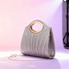 Silberglitzernde plissierte Handtasche mit goldfarbener Schnalle und Perlenkette auf lila Oberfläche.