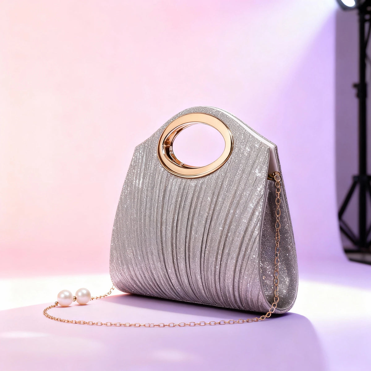 Silberglitzernde plissierte Handtasche mit goldfarbener Schnalle und Perlenkette auf lila Oberfläche.
