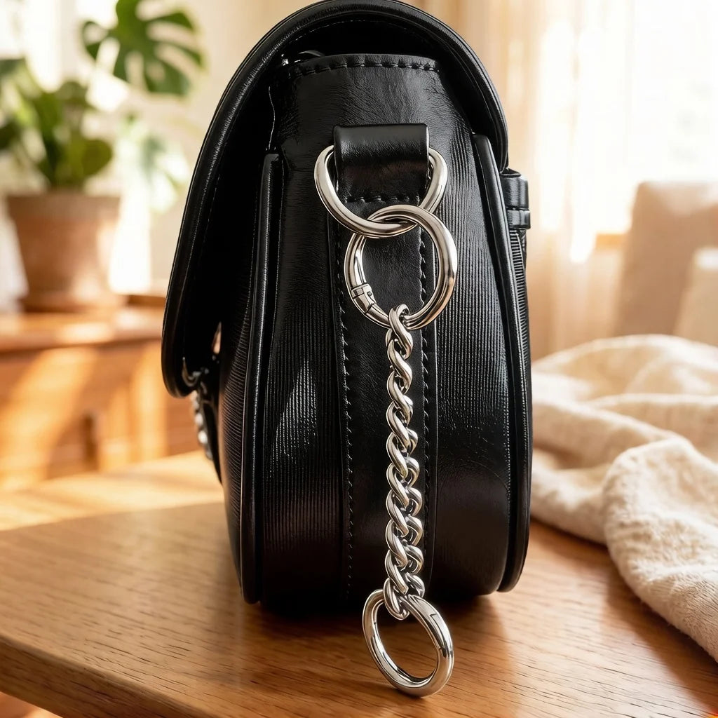 Black leather handbag with a silver metal strap extender chain resting on a wooden surface.