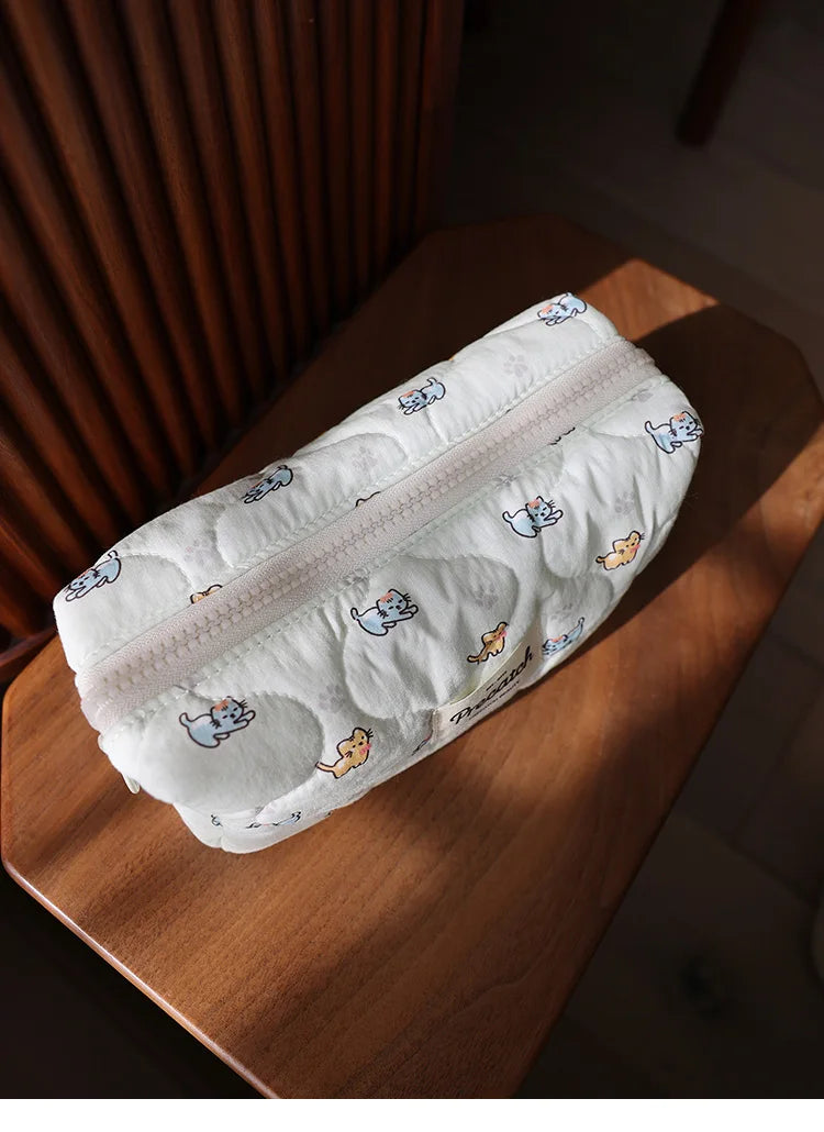 A white cosmetic storage pouch with a light pattern of cute cats resting on a wooden surface.