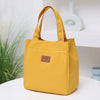 A mustard yellow durable aluminum foil insulated lunch bag with woven handles resting on a white surface.