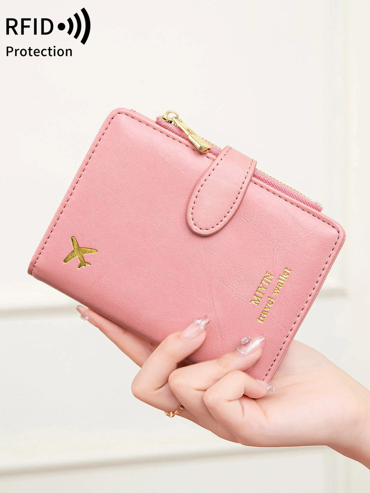 A hand holds a pink multi-functional PU leather passport wallet with gold accents and a small airplane emblem.