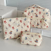 A set of quilted cotton makeup organizers in cream fabric featuring small animal embroidery and red ribbon details.