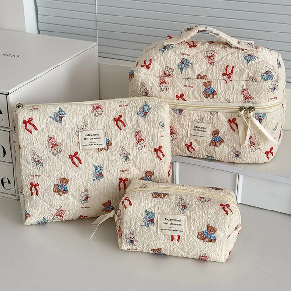 A set of quilted cotton makeup organizers in cream fabric featuring small animal embroidery and red ribbon details.