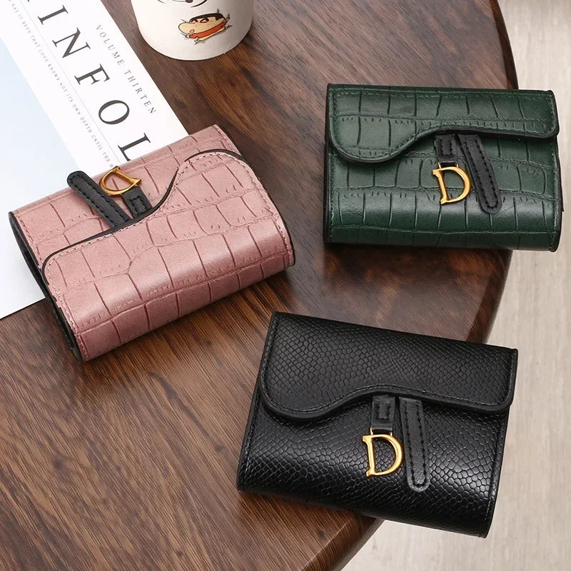 Collection de trois porte-cartes de luxe en cuir rose, vert et noir sur une surface en bois.