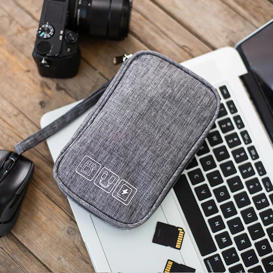 A gray portable digital organizer storage pouch resting on a wooden surface next to a laptop and camera.