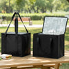 A black reusable insulated cooler bag with a lid is placed on a wooden table outdoors.