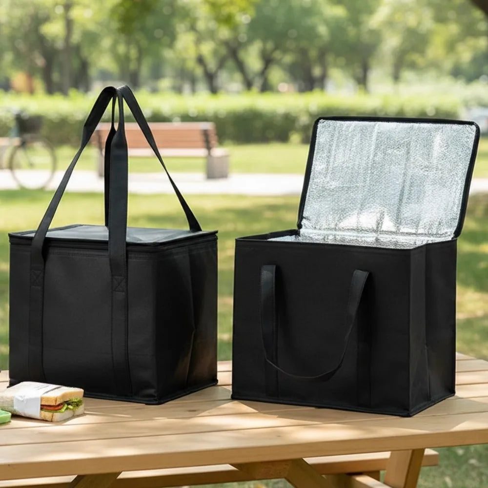 A black reusable insulated cooler bag with a lid is placed on a wooden table outdoors.