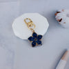 A gold-toned flower resin keychain with blue petals rests on a white ceramic tile.