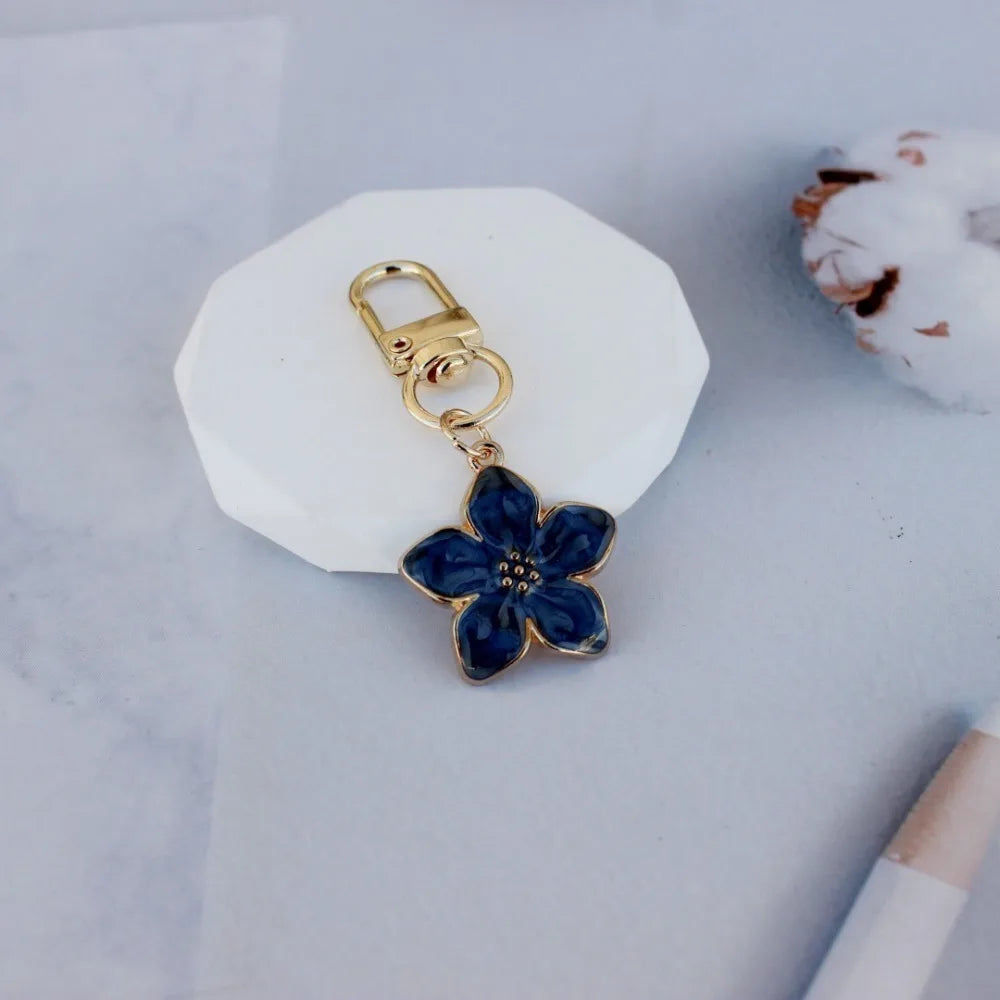 A gold-toned flower resin keychain with blue petals rests on a white ceramic tile.