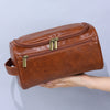 Braune Vintage PU-Leder-Toiletrytasche mit Reißverschluss und Aufhänger, gehalten von einer Hand.