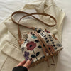 A close-up of a floral drawstring bucket bag in beige and brown tones resting on a light cream blazer.