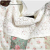Close-up of a white crocheted lace scarf or shawl with pink floral details, displayed against a patchwork fabric background.