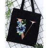 Black canvas tote bag featuring a gold foil alphabet V design and blue floral print