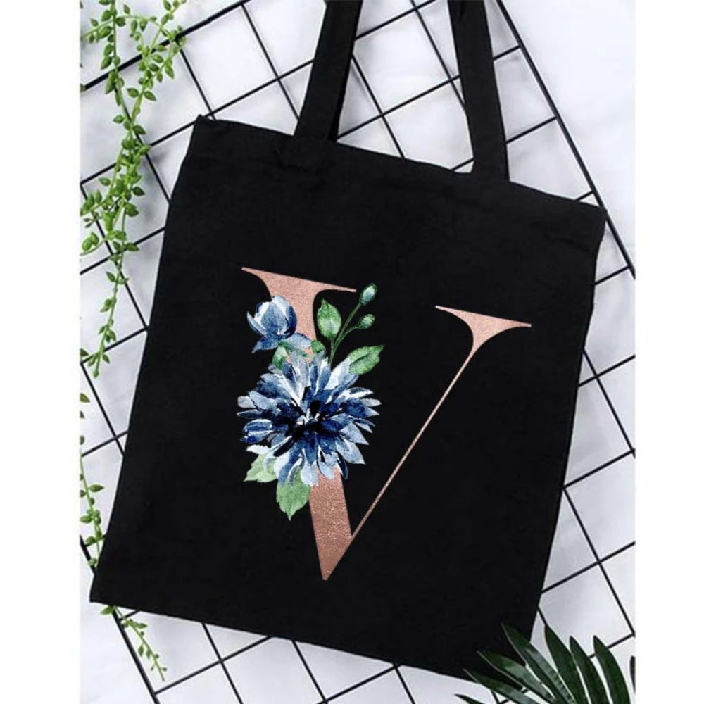 Black canvas tote bag featuring a gold foil alphabet V design and blue floral print