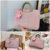 A pink quilted laptop sleeve with a green handle and pink floral charm is shown being held by a hand.