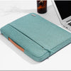 A teal laptop sleeve with a handle is shown resting on a white surface next to a dark glass.