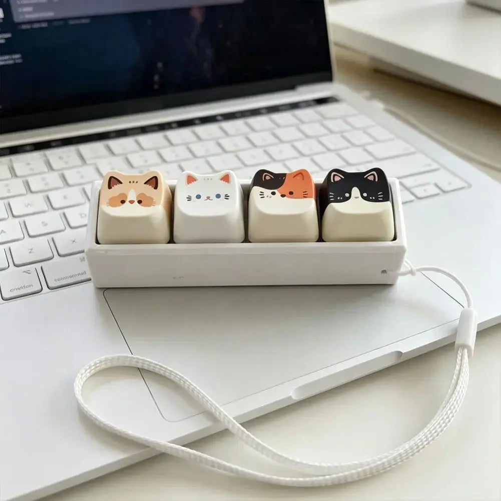 A white plastic tray holds five cat-shaped keycap fidget toys with white and orange designs, resting on a laptop.
