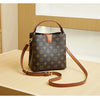 A brown leather bucket bag with gold hardware and a tan strap resting on a light wooden surface.