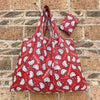 A red fabric shopping bag patterned with white cat faces, displayed against a stone brick wall.