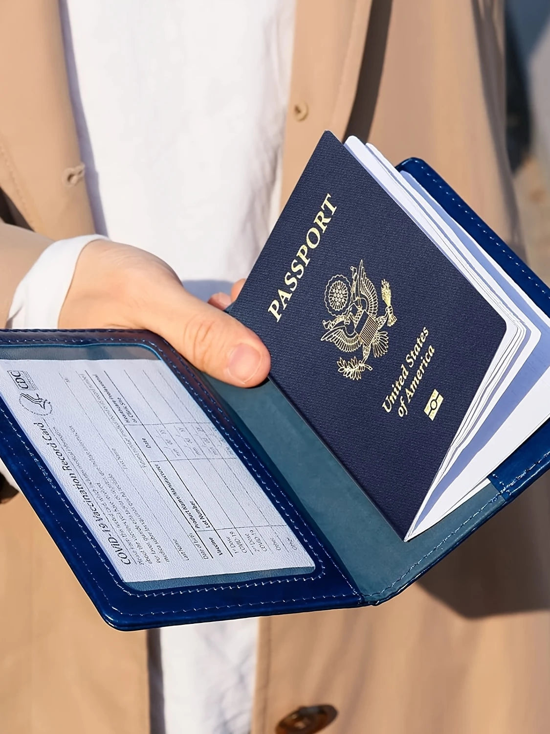 A hand holds a navy blue passport holder wallet with a gold embossed United States passport inside.