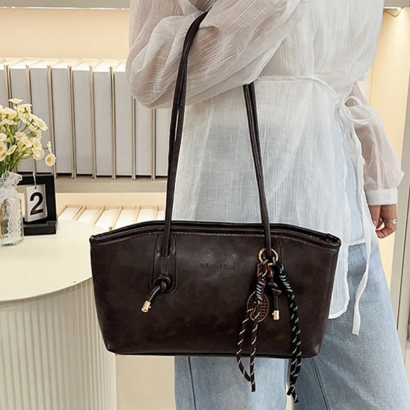 A woman holds a dark brown classic PU leather tote bag with a long strap in front of a white background.