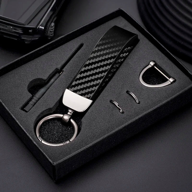 A black box holds a carbon fiber leather keychain with a silver finish and a small tool.
