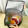 A hand is opening a silver foil reusable insulated cooler bag revealing fresh fruits and vegetables inside.