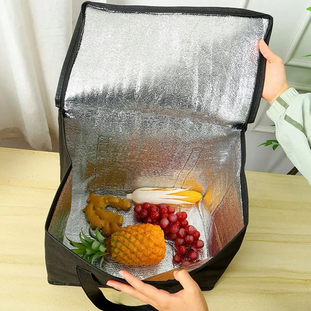 A hand is opening a silver foil reusable insulated cooler bag revealing fresh fruits and vegetables inside.