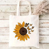 A white canvas tote bag featuring a yellow and black butterfly sunflower print on a light wooden background.