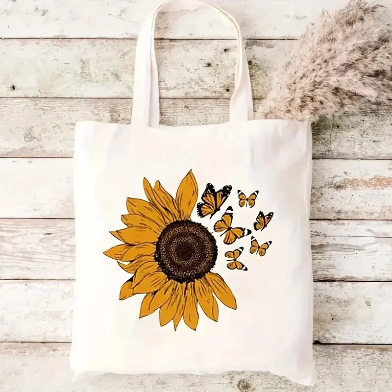 A white canvas tote bag featuring a yellow and black butterfly sunflower print on a light wooden background.