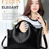 A woman models a black luxury soft leather tote bag in a studio setting.