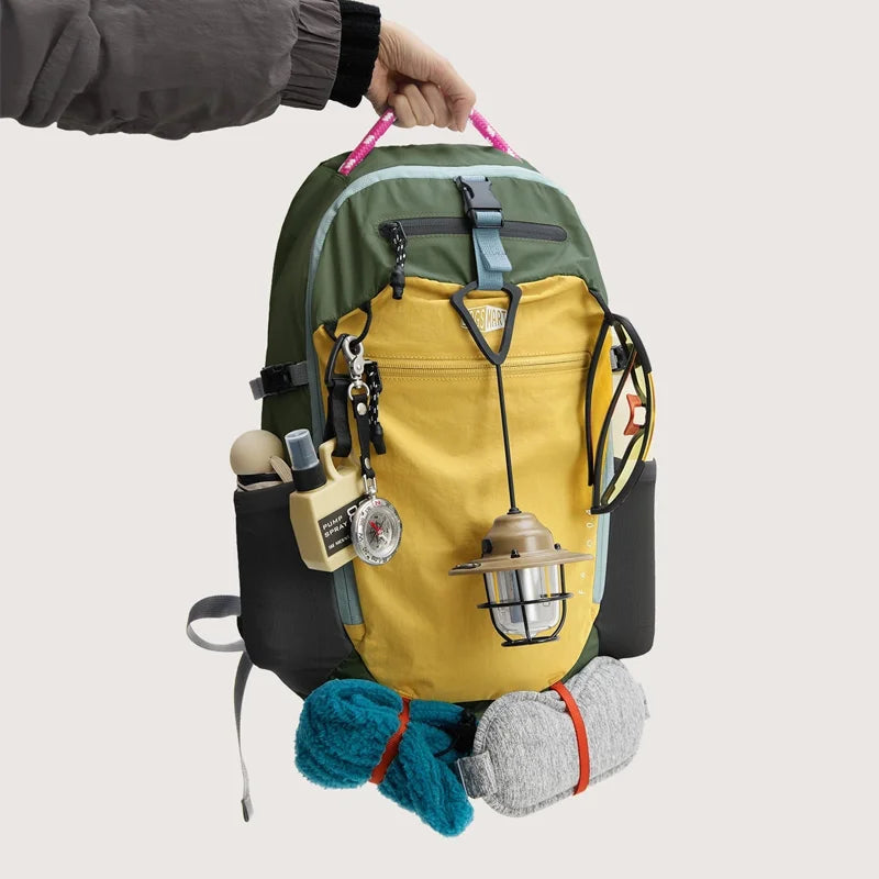 A yellow and green durable laptop backpack with various tools and gear attached, held by a hand.