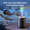 A black humidification device is placed on a wooden table next to a woman sleeping in bed.