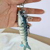 A silver-colored simulation fish charm hanging from a chain and attached to a gold-colored keyring.
