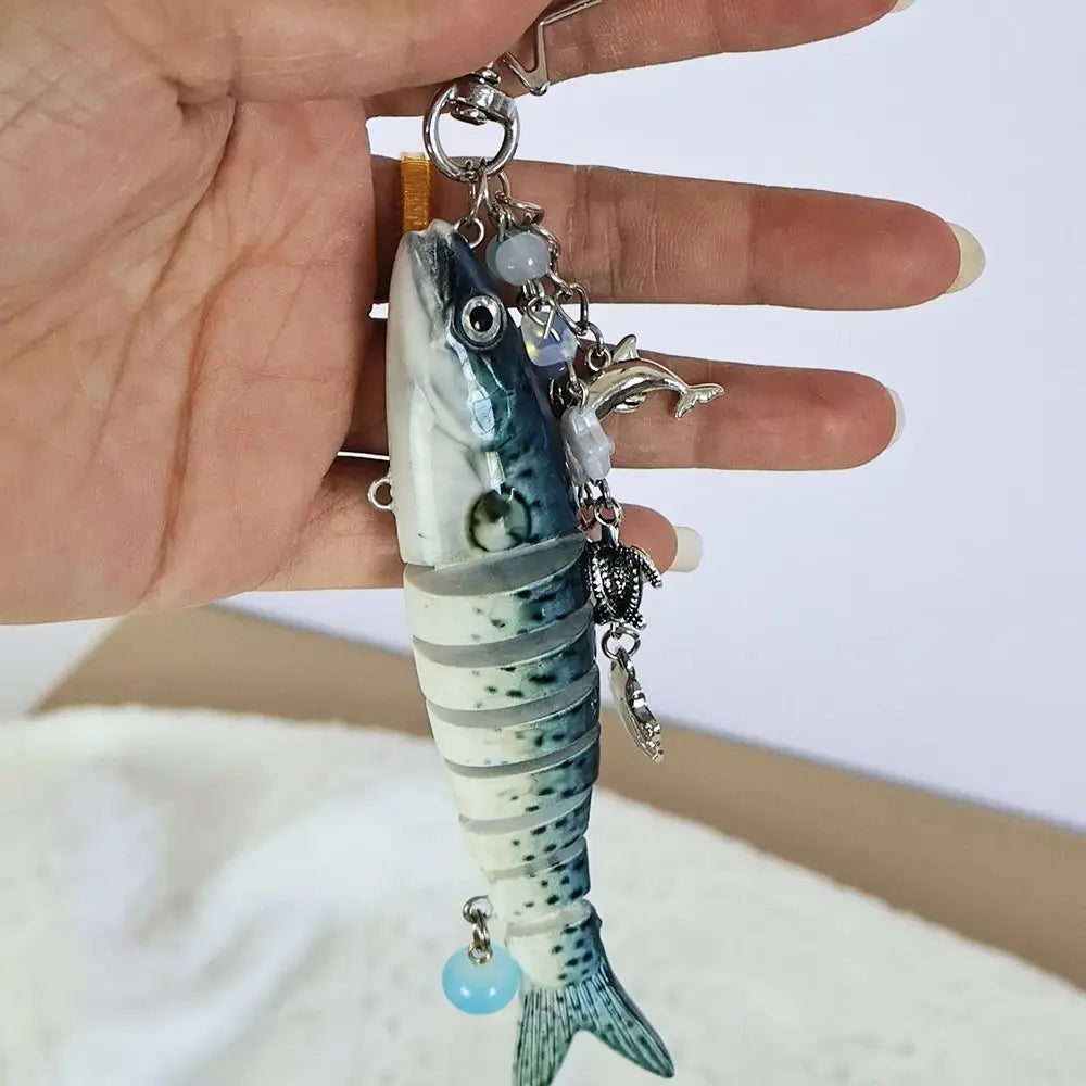 A silver-colored simulation fish charm hanging from a chain and attached to a gold-colored keyring.