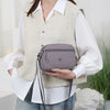 A woman wearing a cream vest and white shirt holds a mauve nylon crossbody bag.