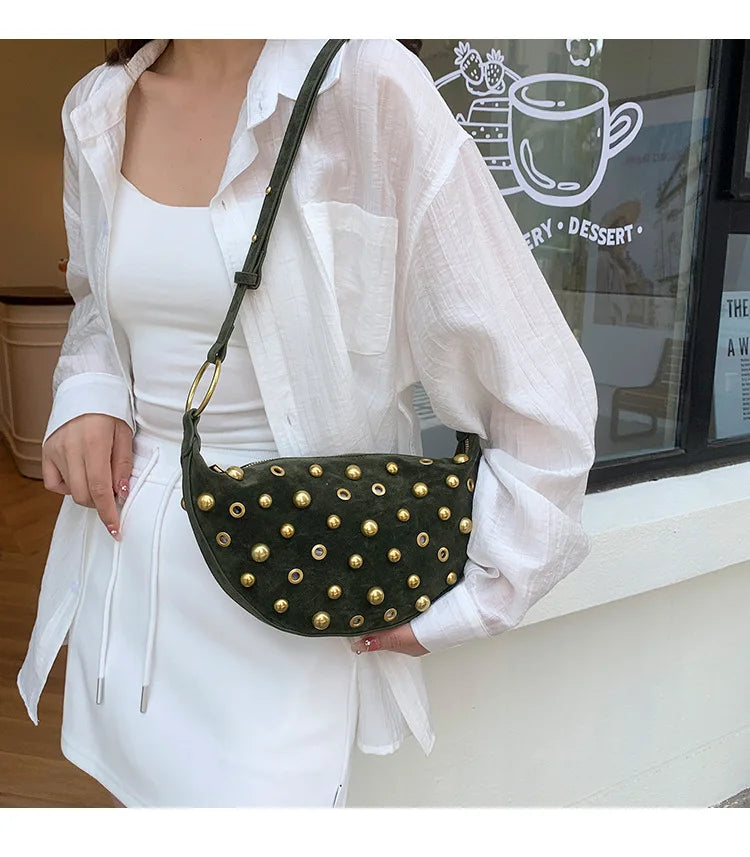 A woman holds a dark green faux suede hobo crossbody bag with gold rivet accents in a white shirt.