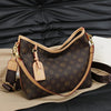 A brown leather crossbody tote bag with a dark brown monogram print resting on a tan fabric against a black leather surface.
