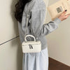 A person holds a cream woven crossbody bag with an adjustable silver chain strap and a light gray sweatshirt.
