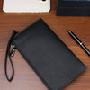 A black clutch bag with a textured surface is placed on a wooden table next to an iPhone.
