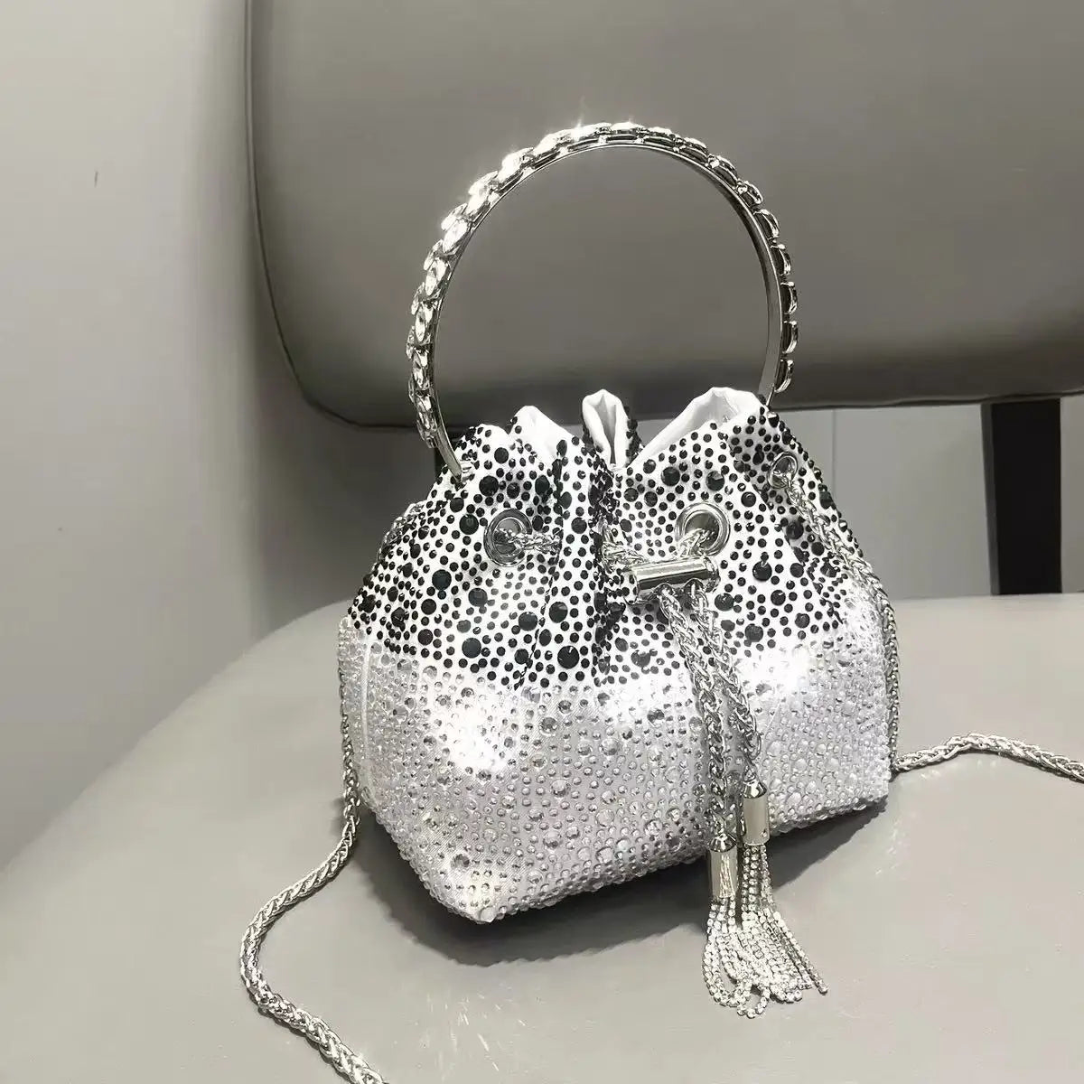 Silver crystal-embellished evening clutch bag with a chain strap resting on a light surface.