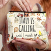A hand holds a cream-colored makeup bag with black text that reads Italy is calling and I must go